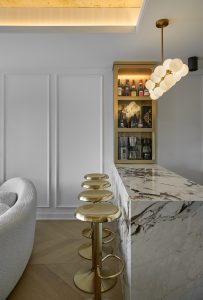 Marble bar and sculptural stools beneath a pendant light and illuminated ceiling recess