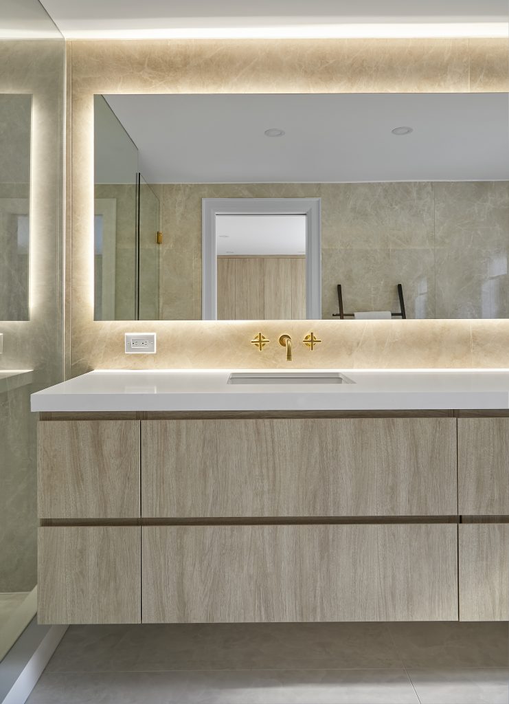 Bathroom vanity with warm lighting around the mirror and beneath the cabinet