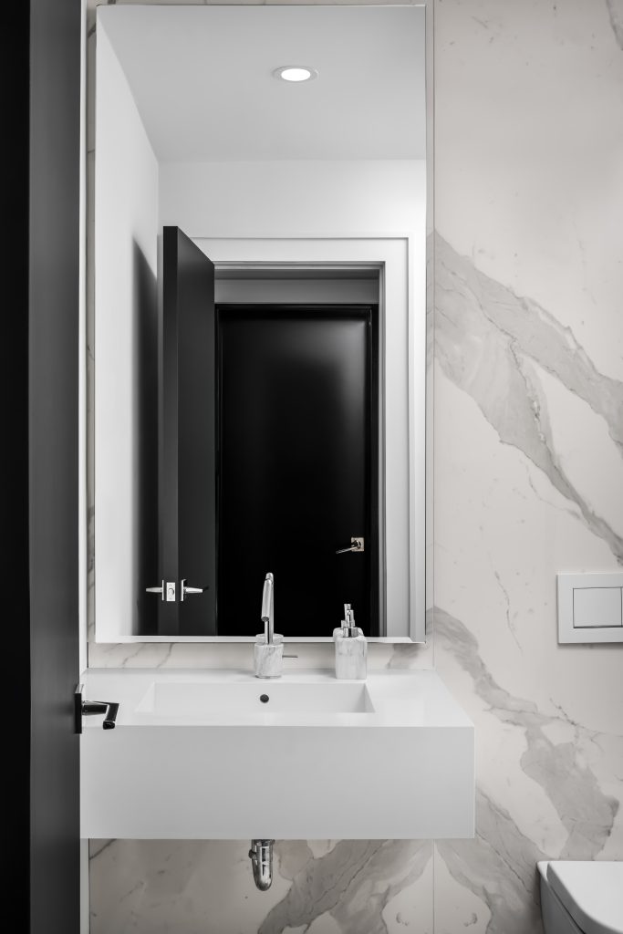 White marble bathroom with dark-framed mirror and recessed ceiling lighting