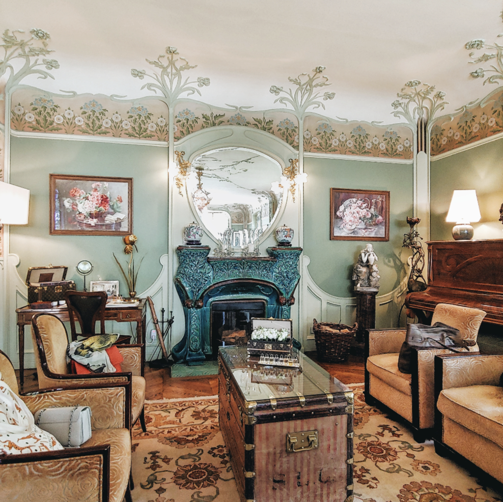 Collected furniture and a travel trunk arranged around an ornate blue fireplace
