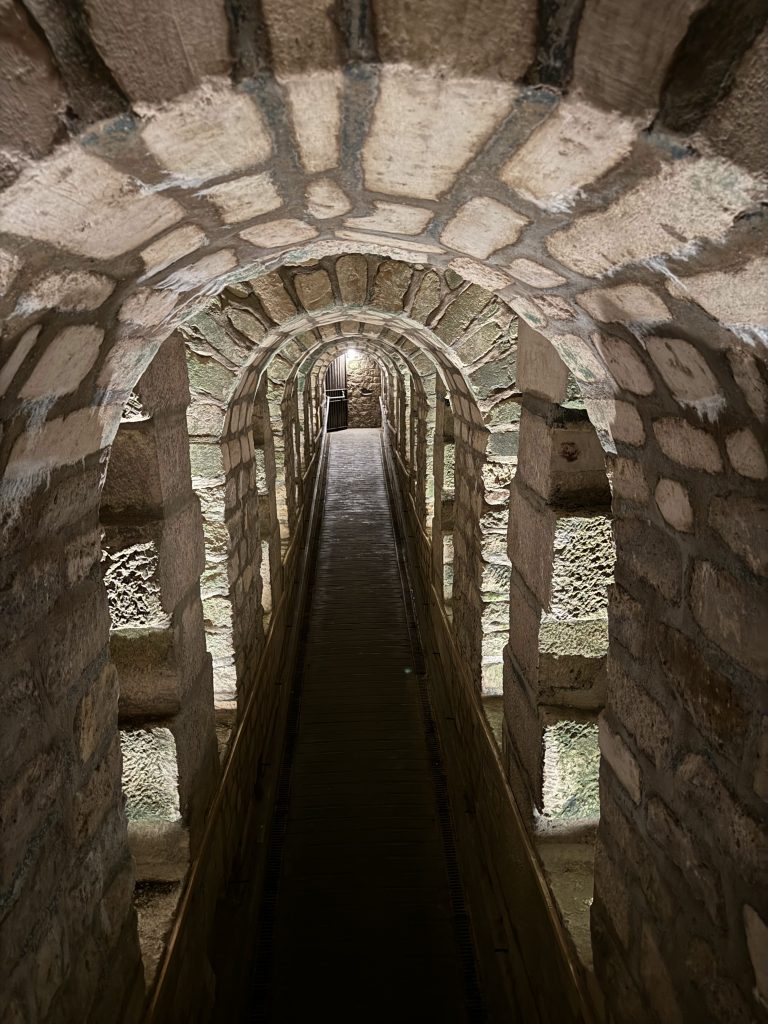 Narrow vaulted stone passage with a central pipe