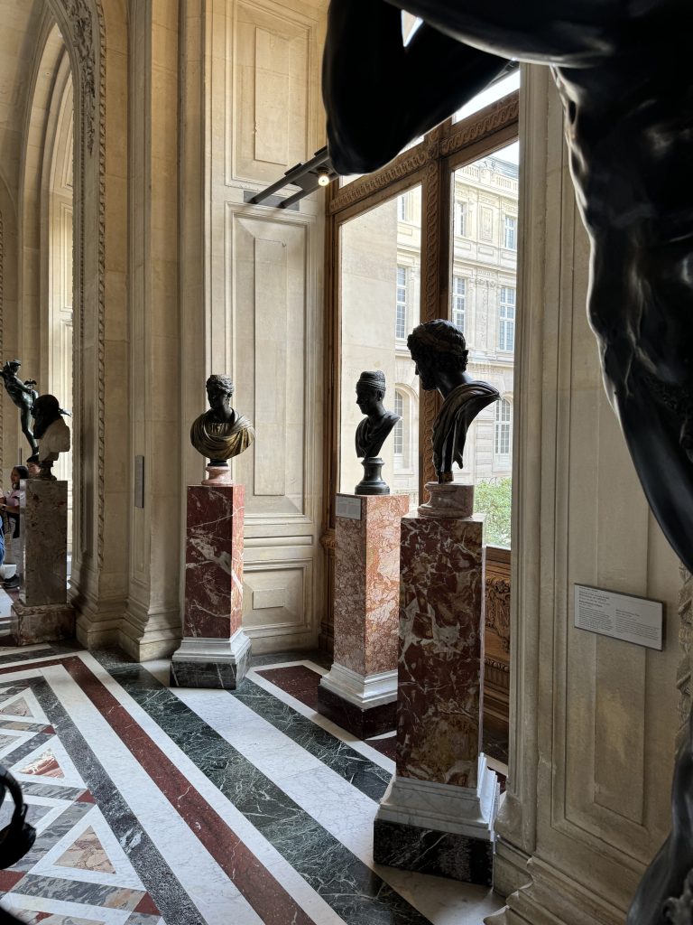 Portrait busts arranged beside tall windows in a marble gallery