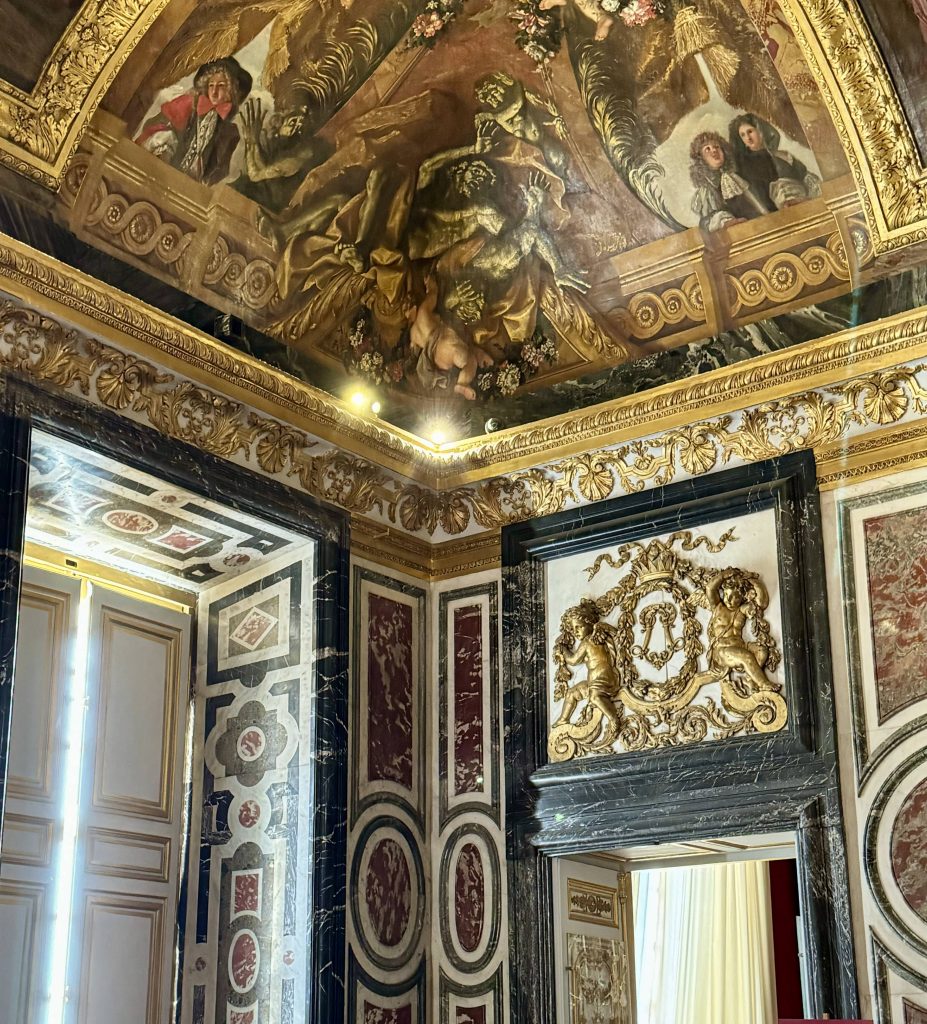 Painted ceiling and richly patterned marble walls inside Versailles