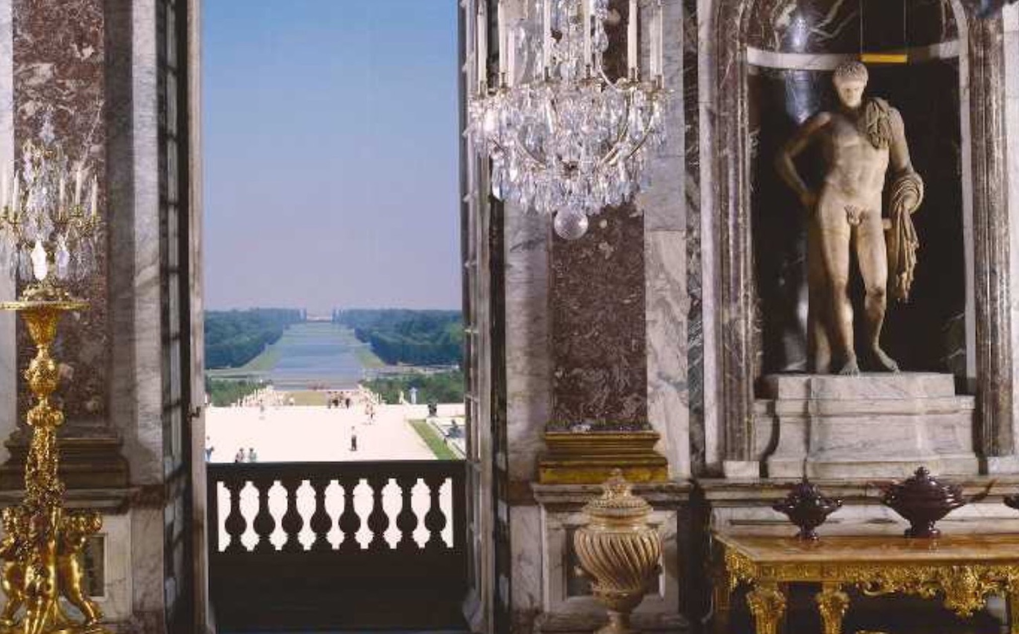 Garden view framed by mirrors, chandeliers and a marble statue
