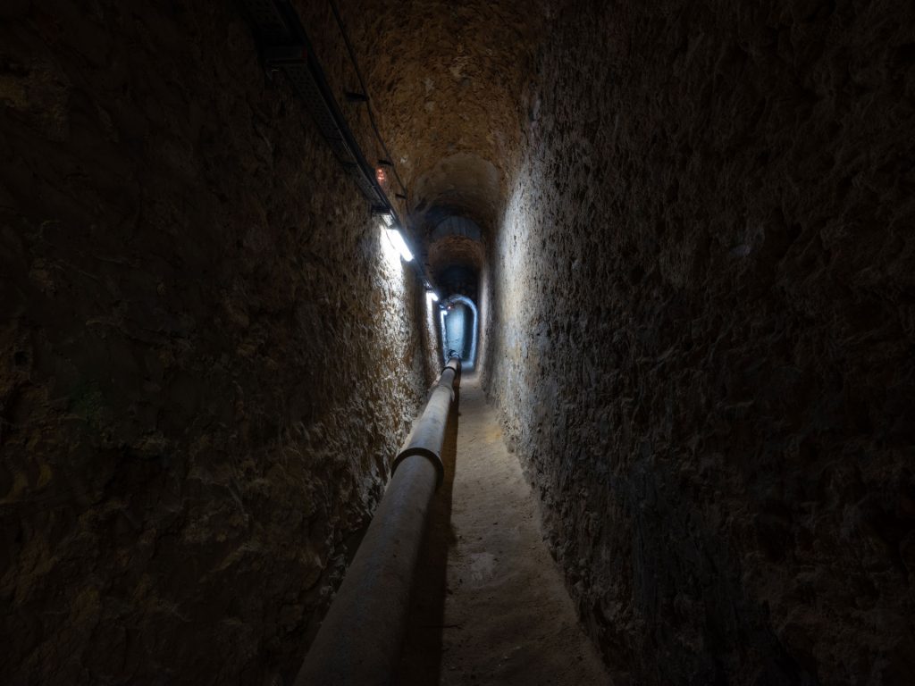 Narrow vaulted stone passage with a pipe running through it
