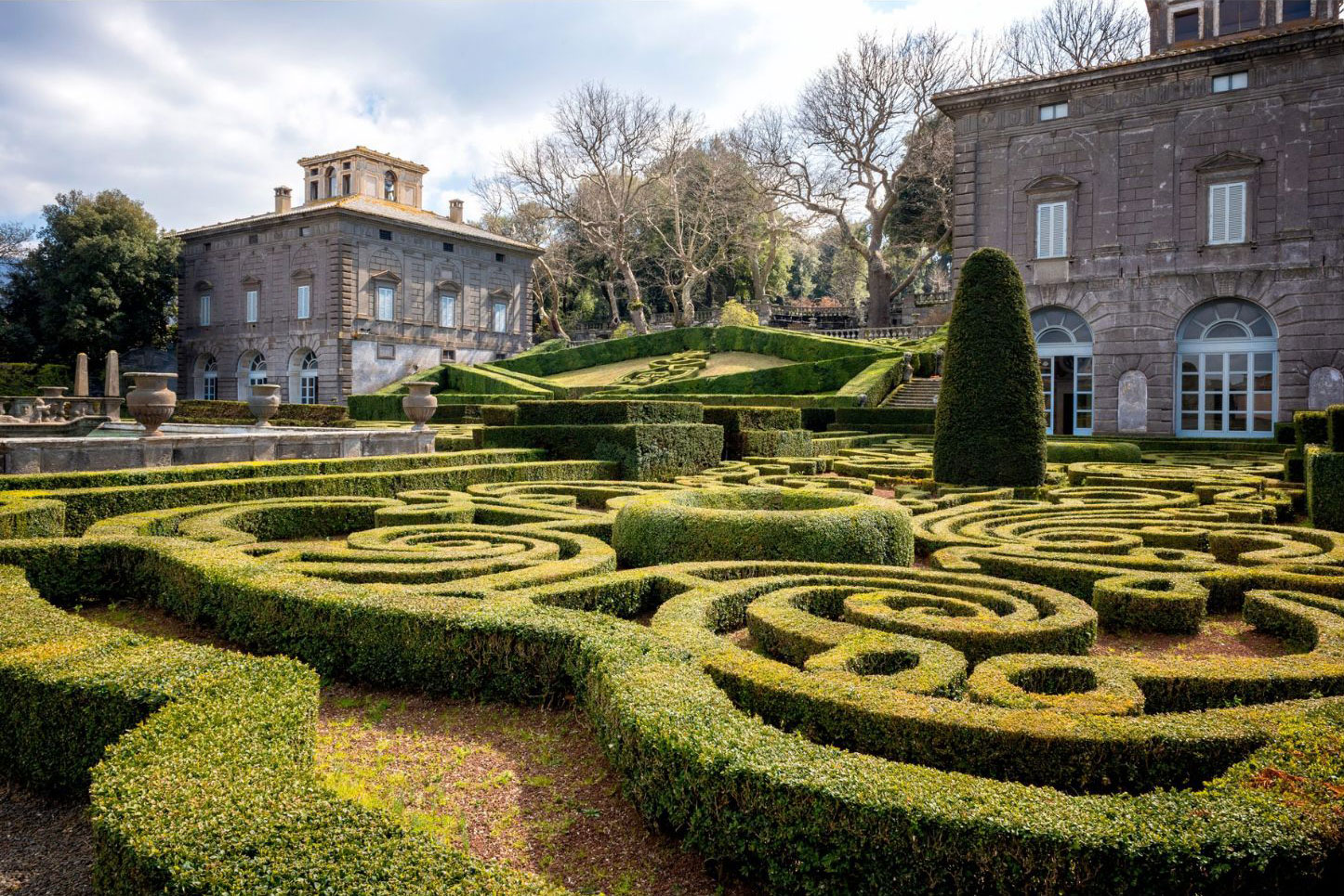 Geometric clipped hedges beside a historic stone house