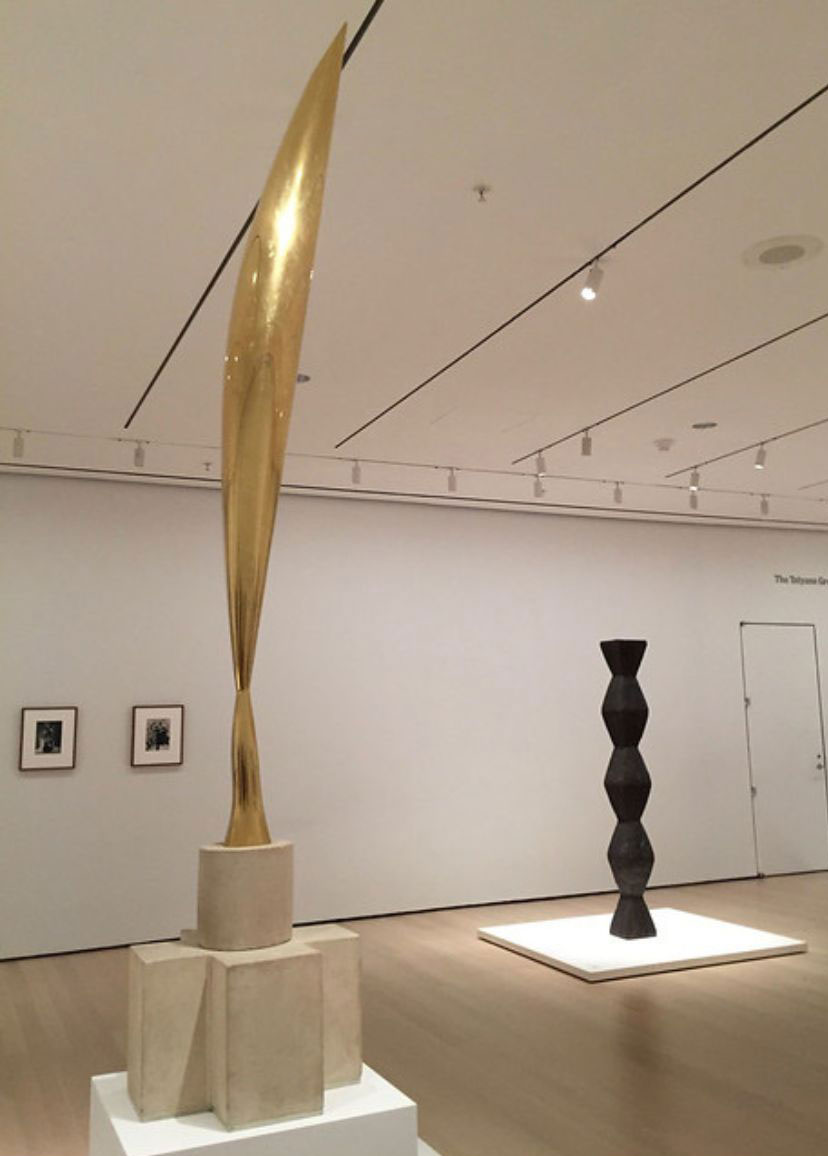 Elongated polished bronze sculpture on a stone pedestal
