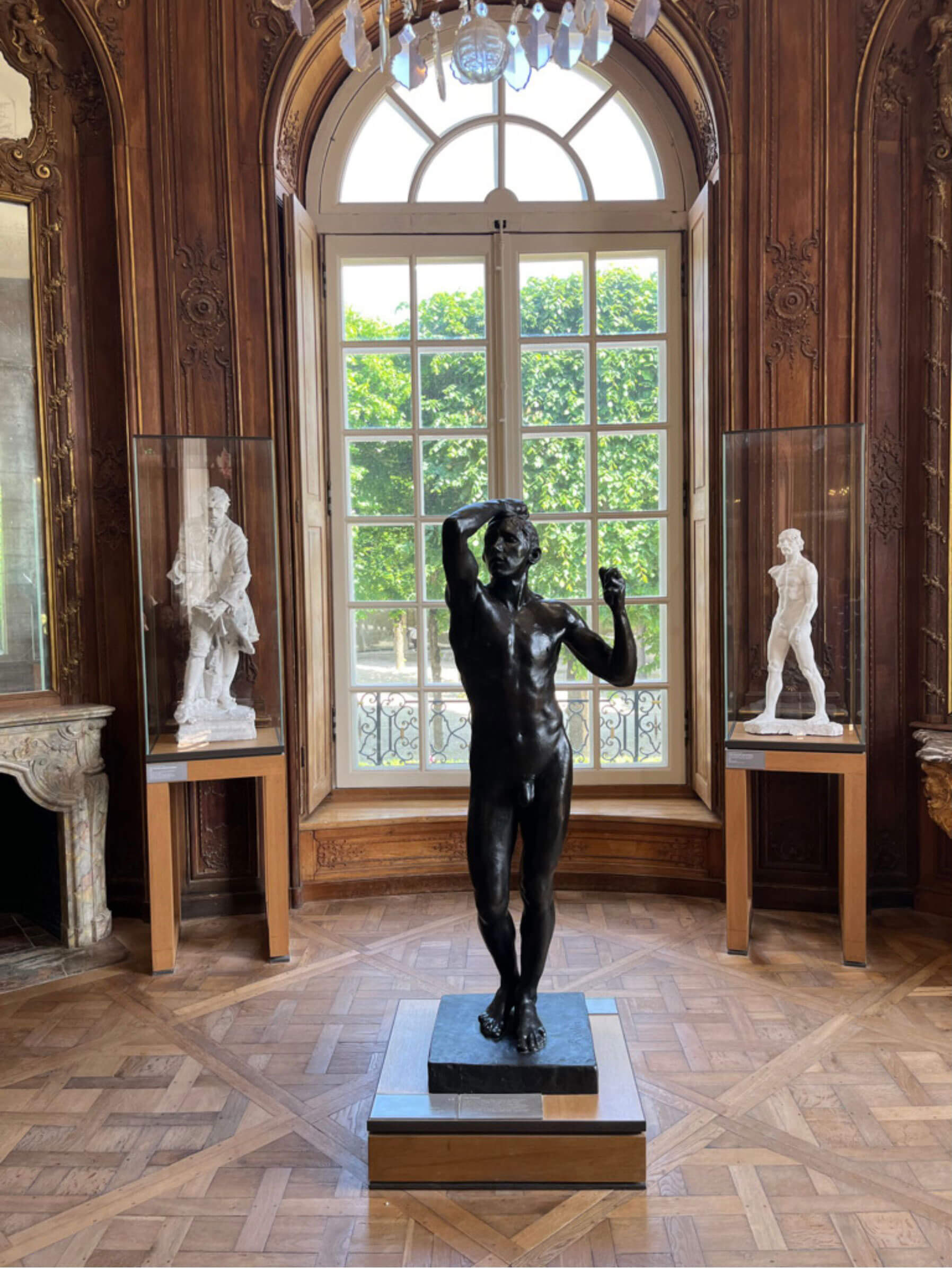 Bronze figure beneath a tall window in an ornate gallery