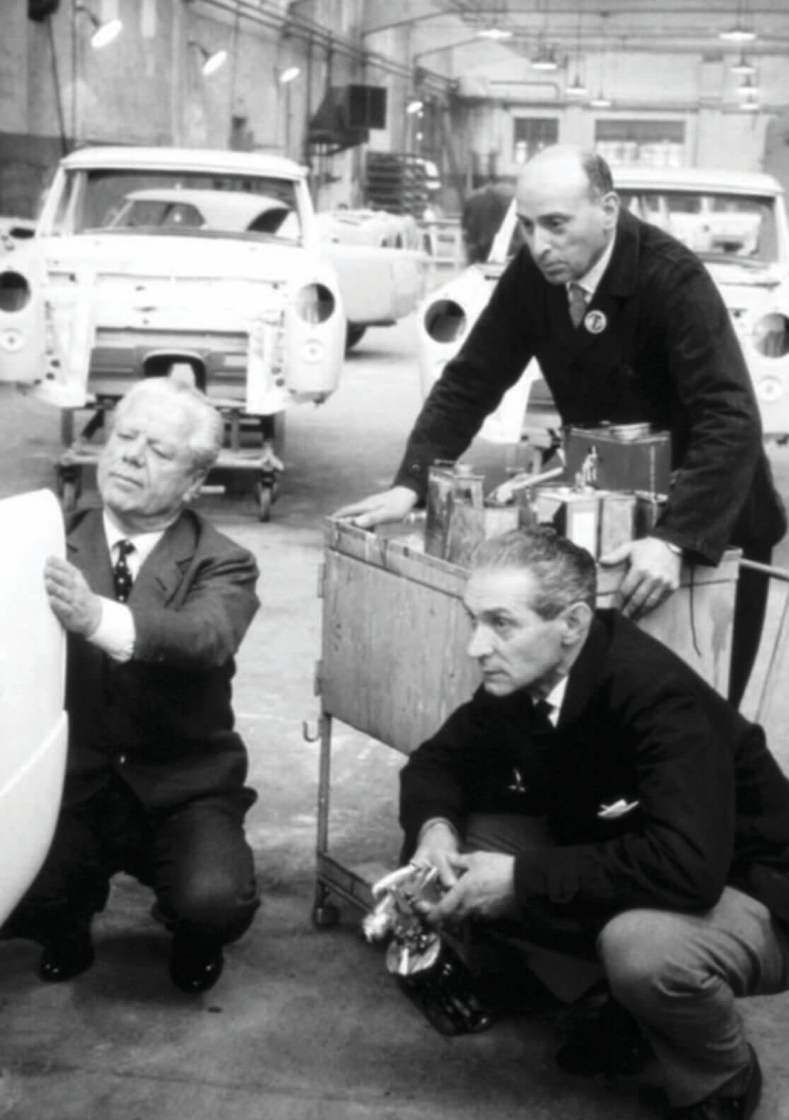 Three men examining a model in an automotive workshop