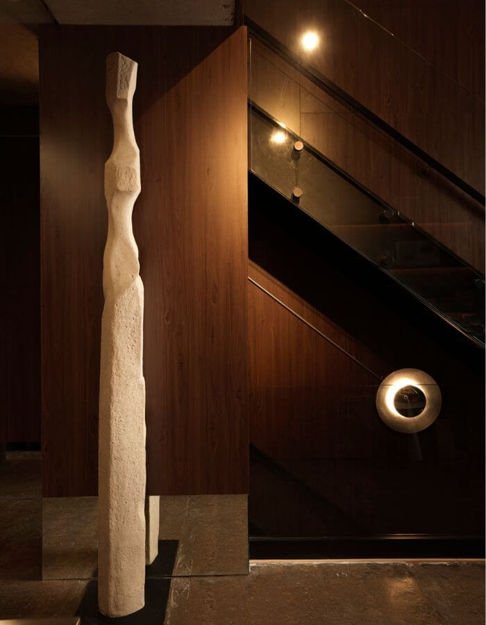 Tall abstract sculpture beside a dark wood staircase in the Sensus studio