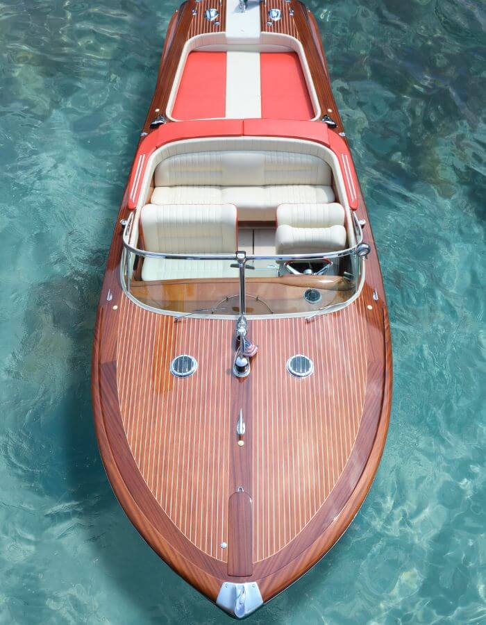 Overhead view of a varnished wooden motorboat with red upholstery on turquoise water