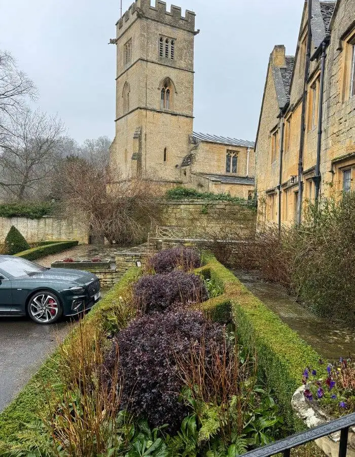 Historic stone buildings and a square tower beside a formal garden
