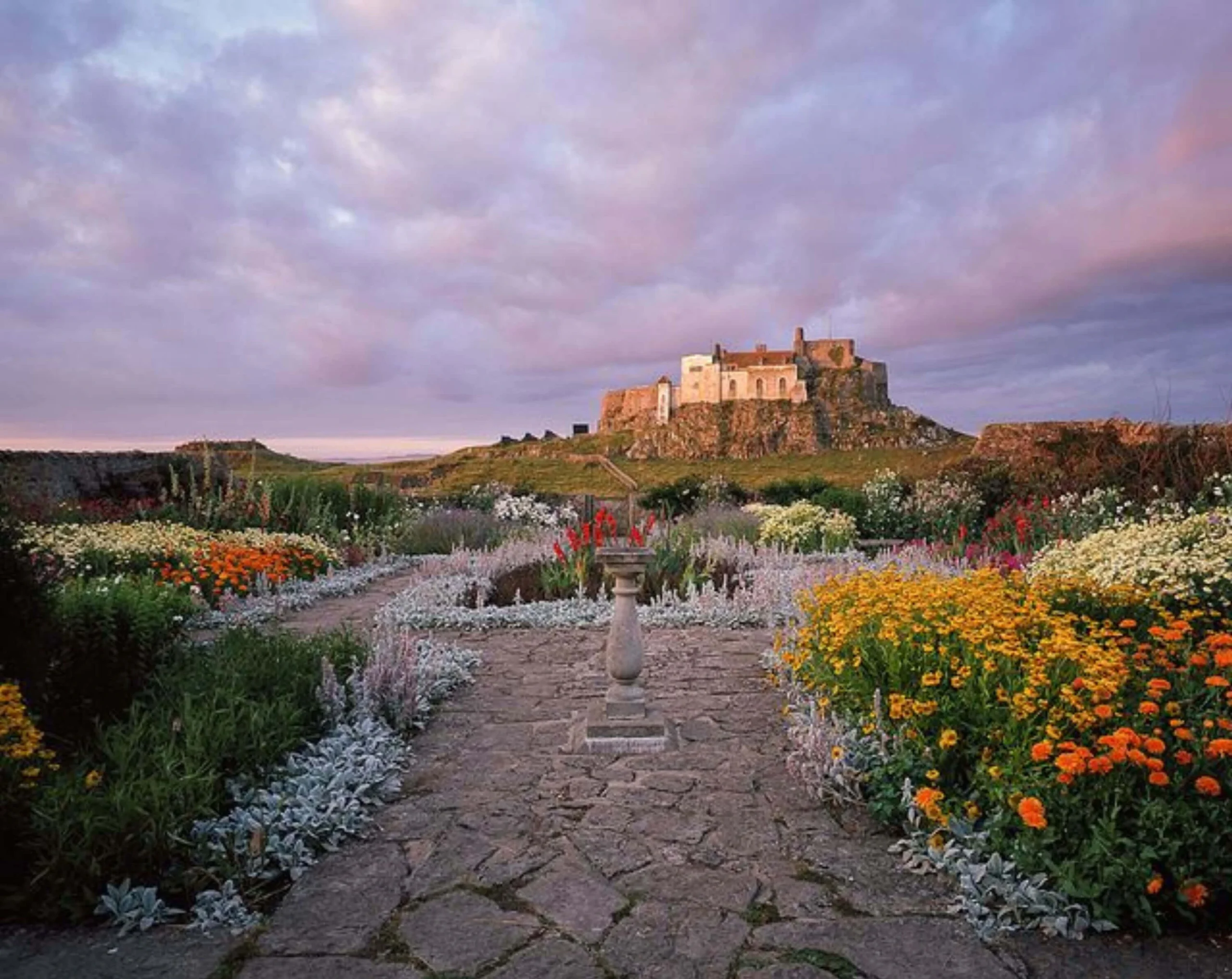 Stone path and flowering borders leading toward a hilltop castle at dusk