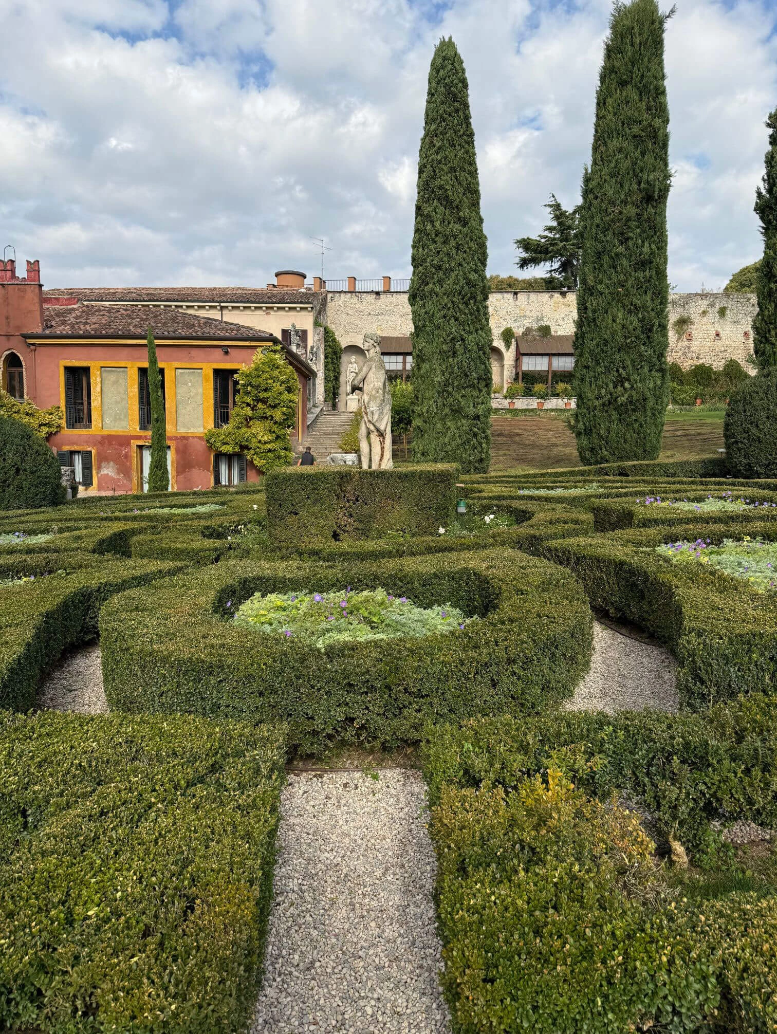 Garden statue and parterres before a warm-toned palazzo