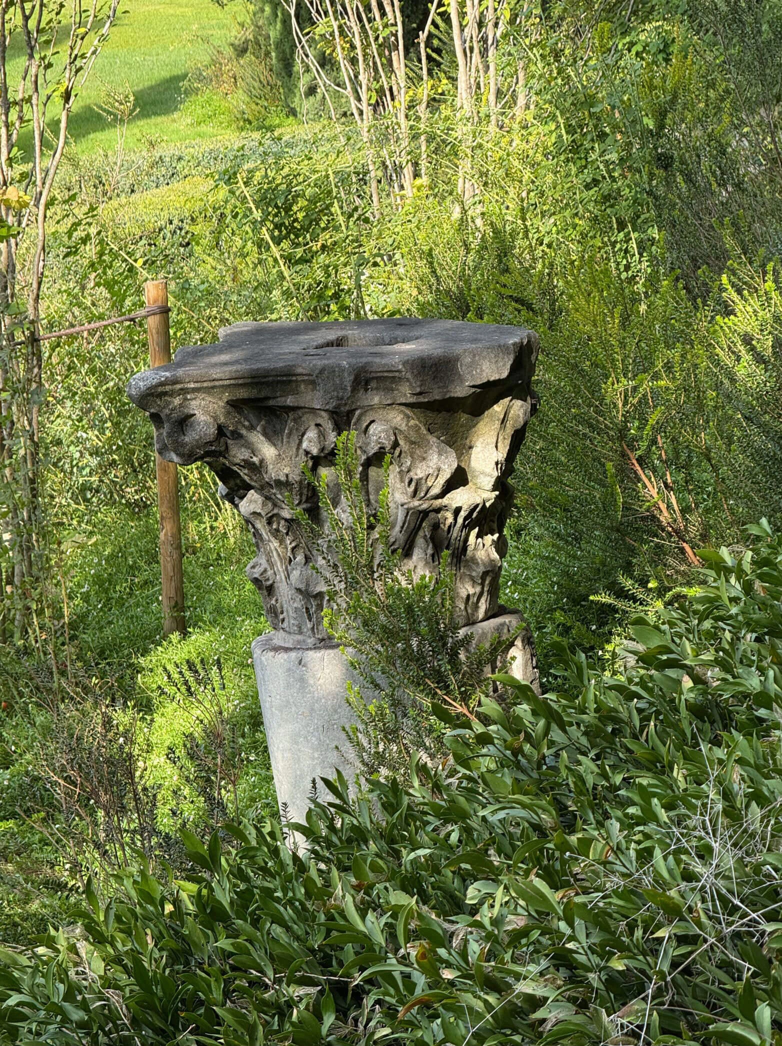 Weathered carved stone capital among hillside greenery