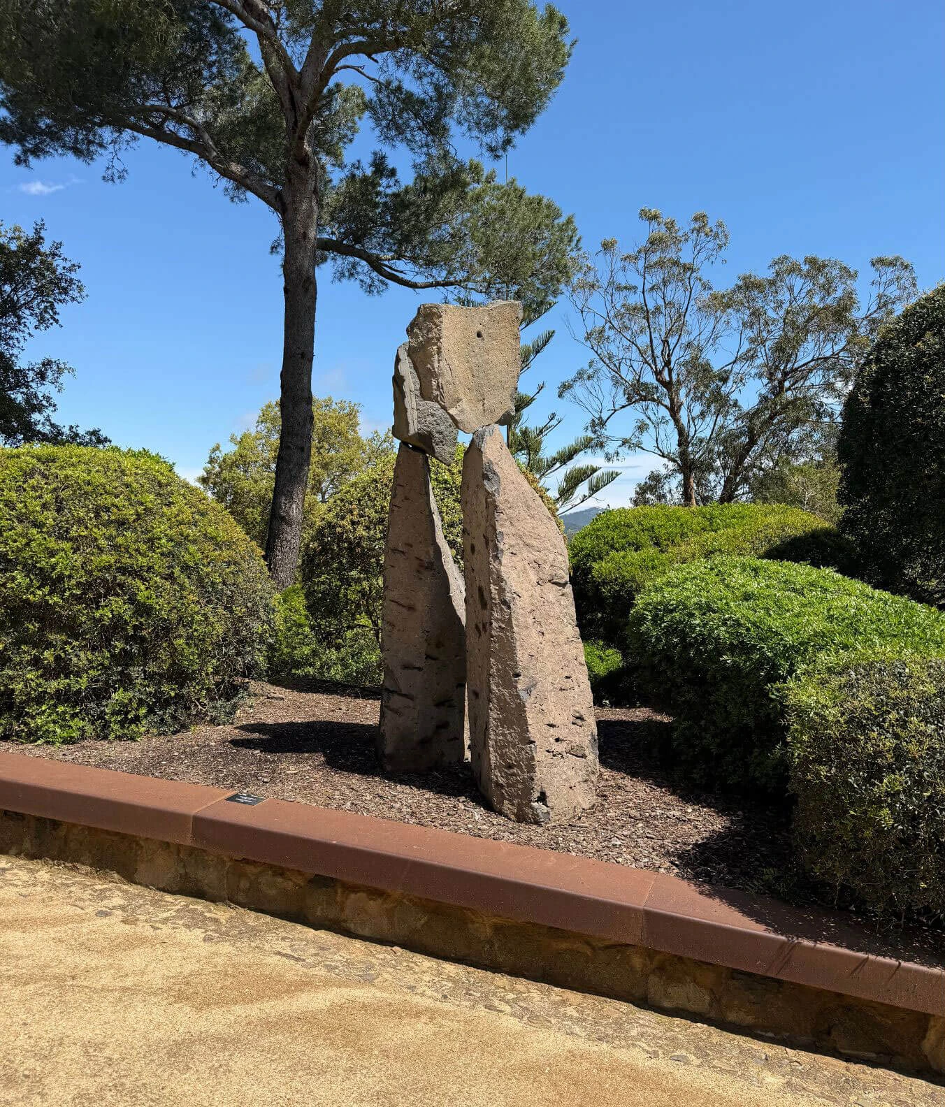 Abstract stone sculpture among clipped shrubs and pine trees