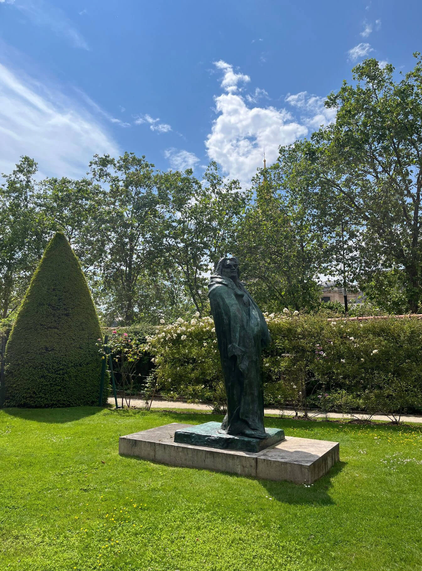 Dark standing figure beside conical topiary
