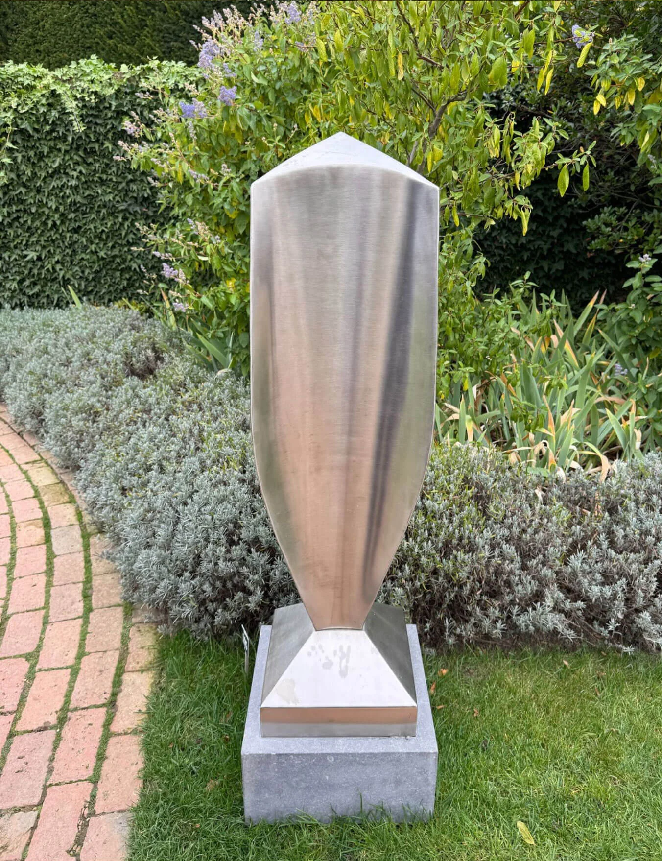 Polished metal sculpture beside a brick garden path