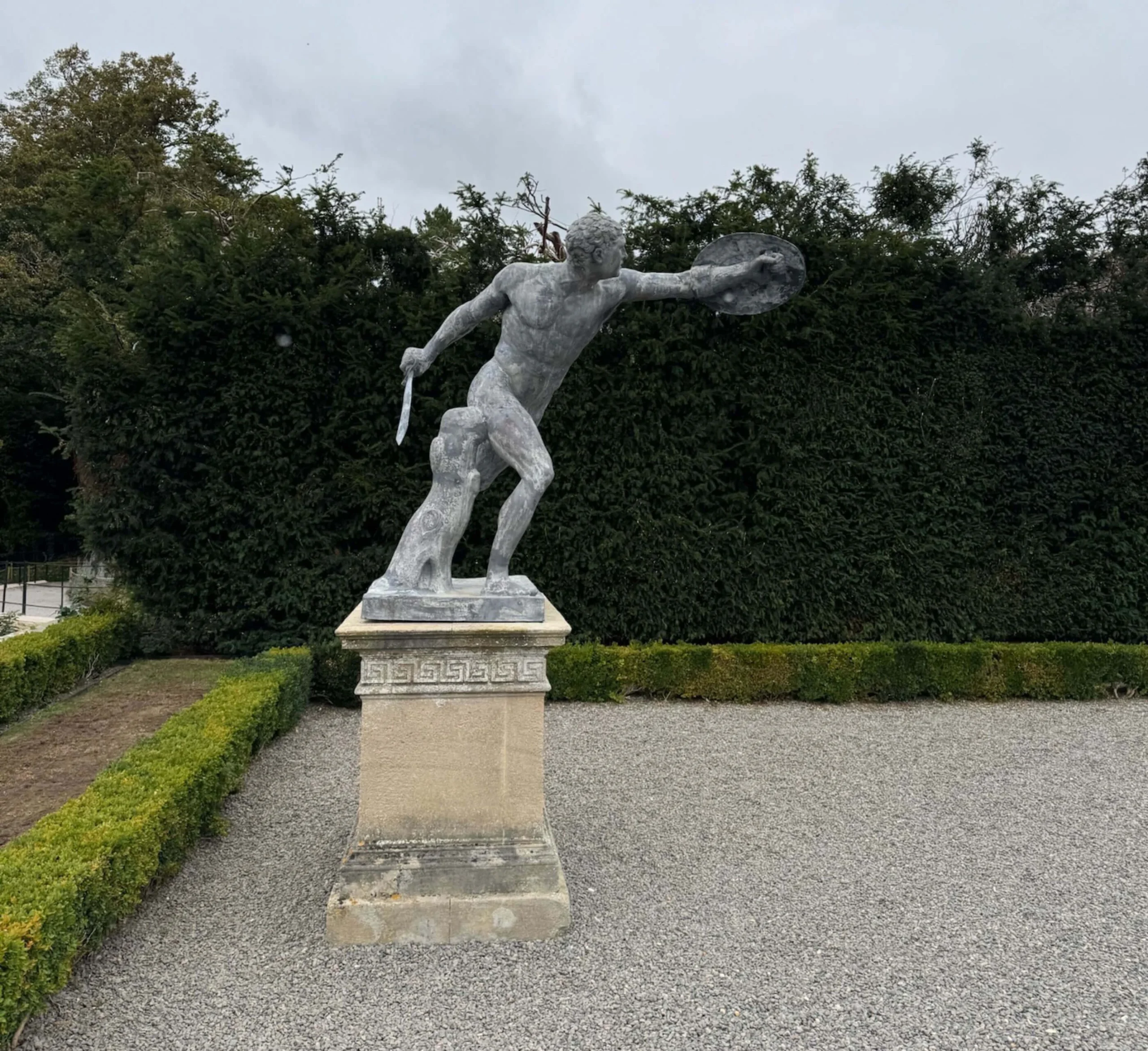 Classical figure extending one arm above a stone plinth