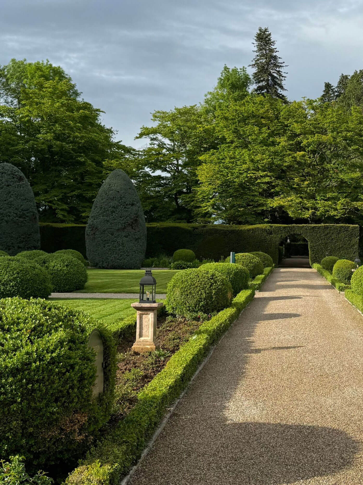 Straight gravel path between low hedges and garden ornaments