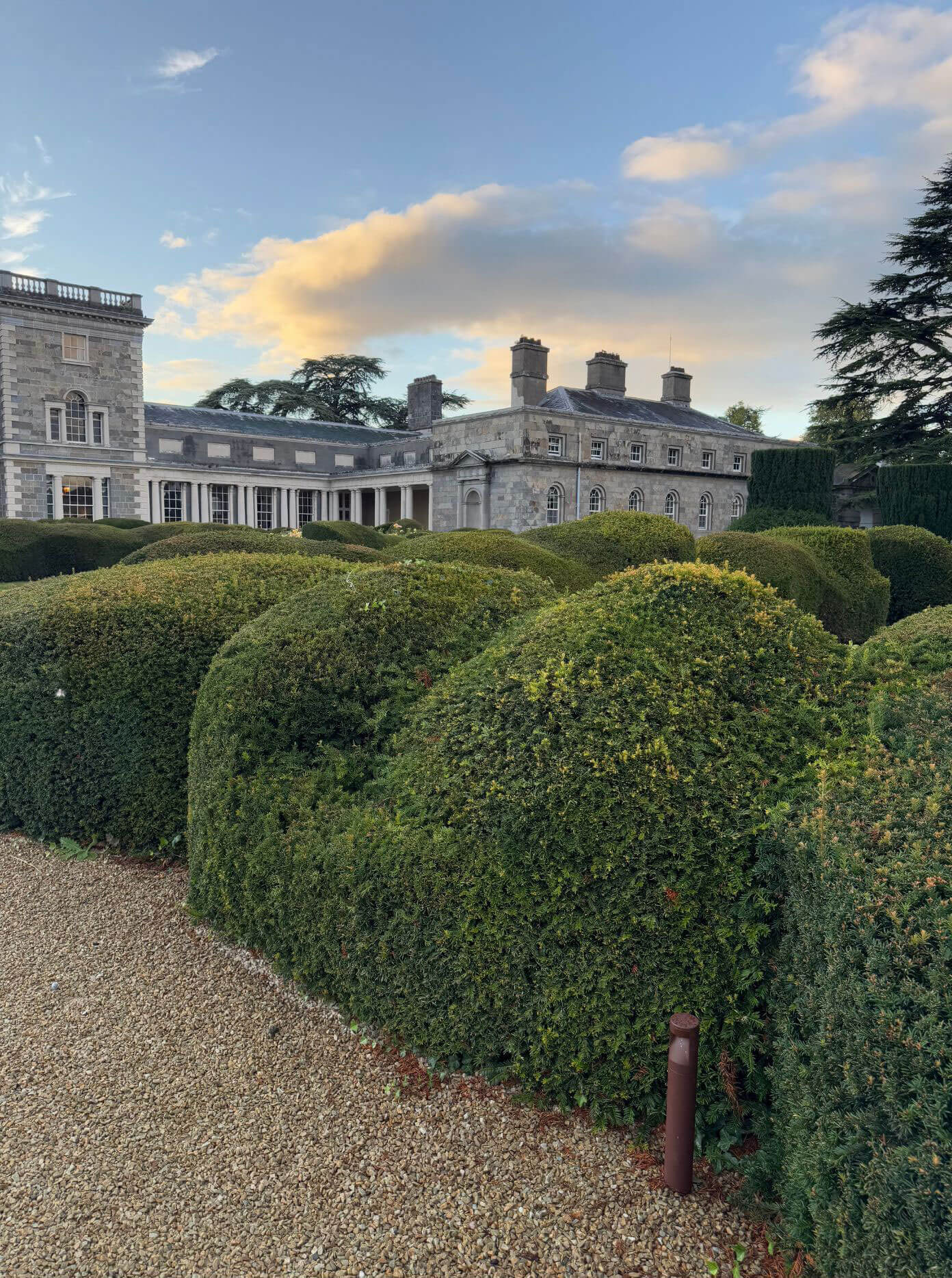 Rounded topiary beside a gravel path overlooking a manor