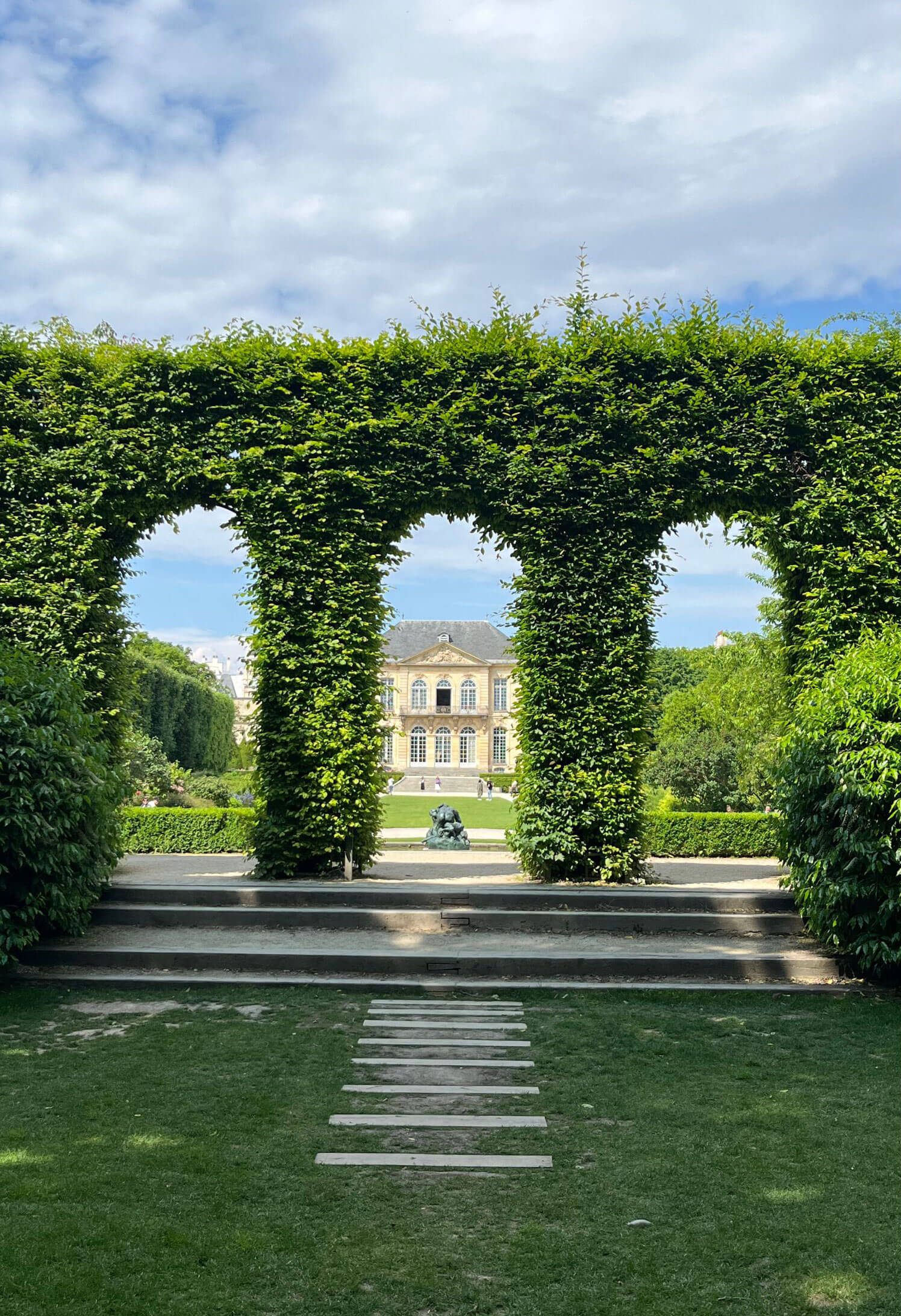 Arched openings cut into a hedge framing a distant house