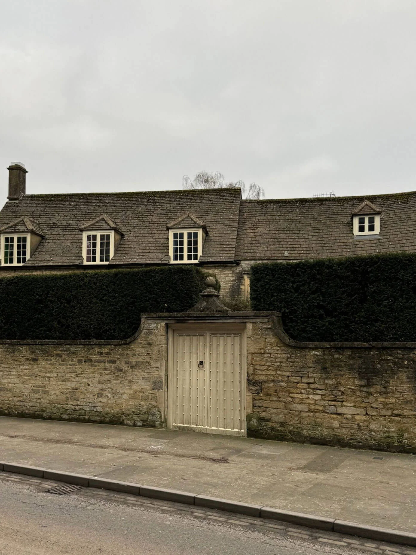 Timber gate between stone walls beneath a dark hedge