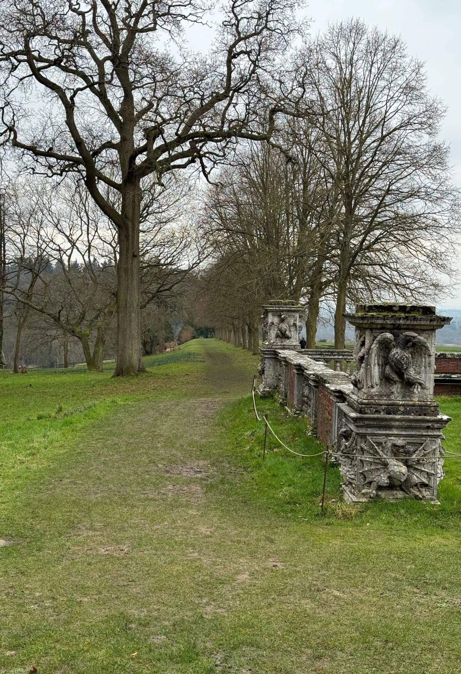 Weathered stone balustrade beside a lawn and trees