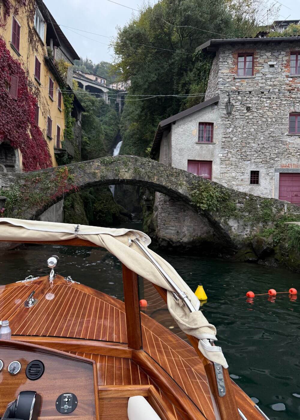Boat bow approaching a small stone bridge between lakeside buildings