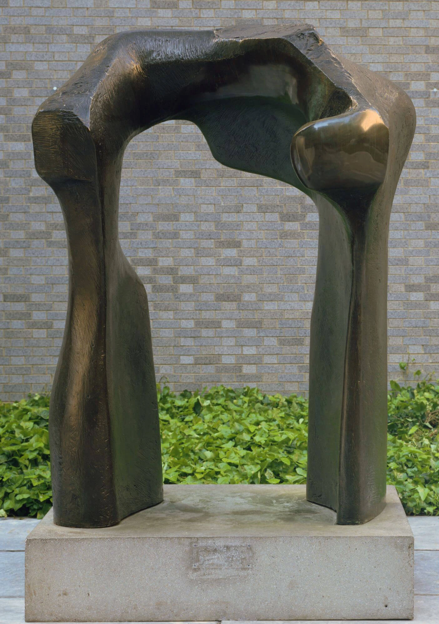 Dark bronze arch on a stone plinth beside a brick wall