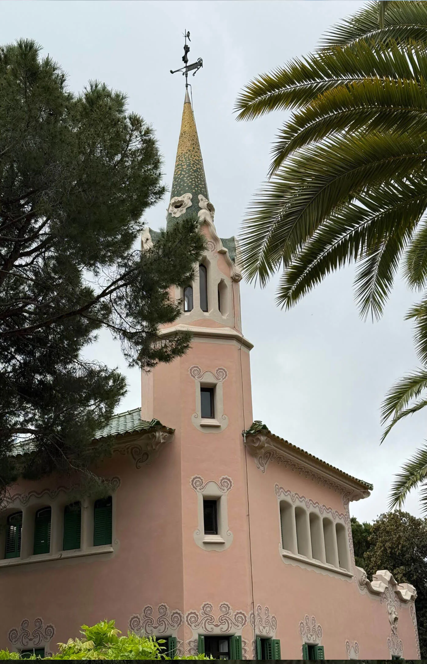 Pink house and slender spire among trees in Park Güell