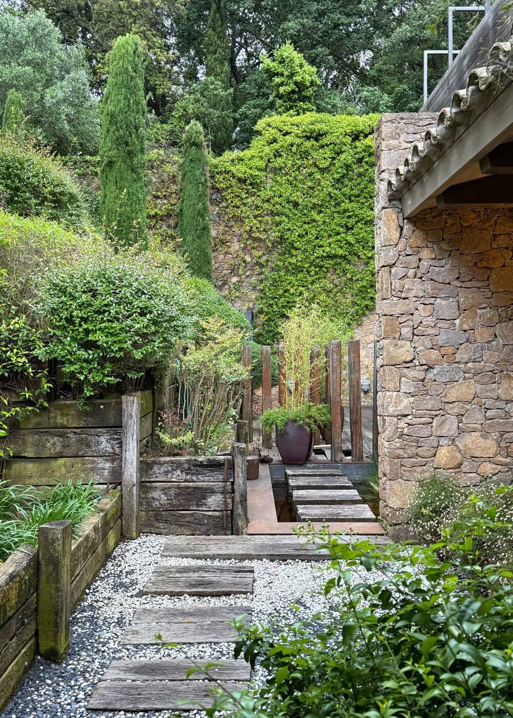 Narrow planted passage and water feature beside a stone building