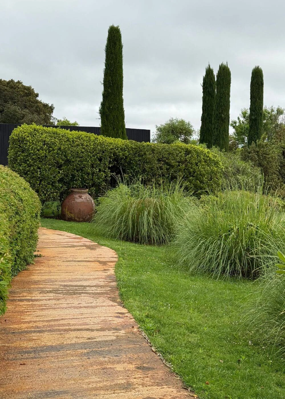 Terracotta garden path beside grasses and clipped hedges