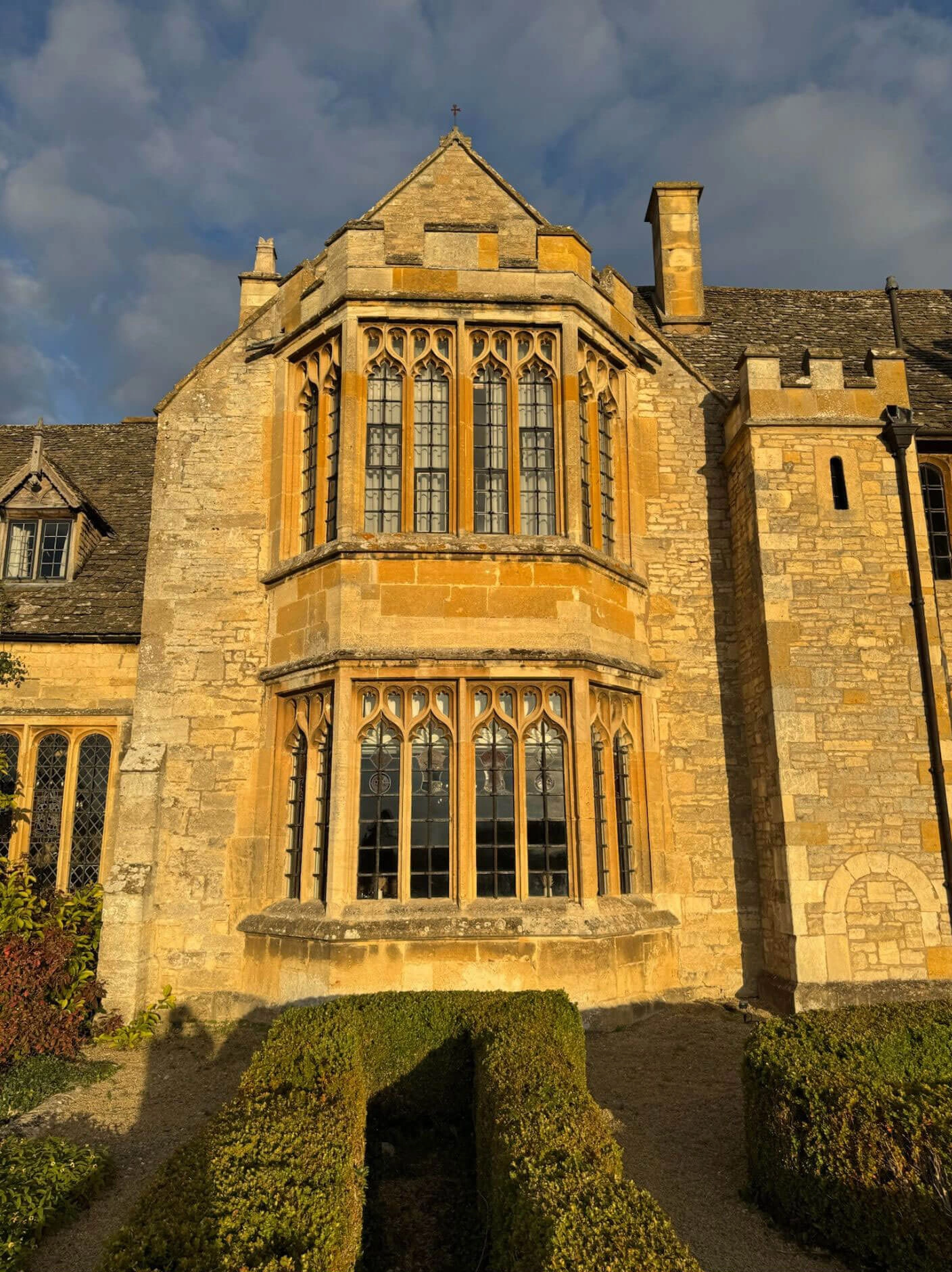 Golden stone bay window above clipped hedges