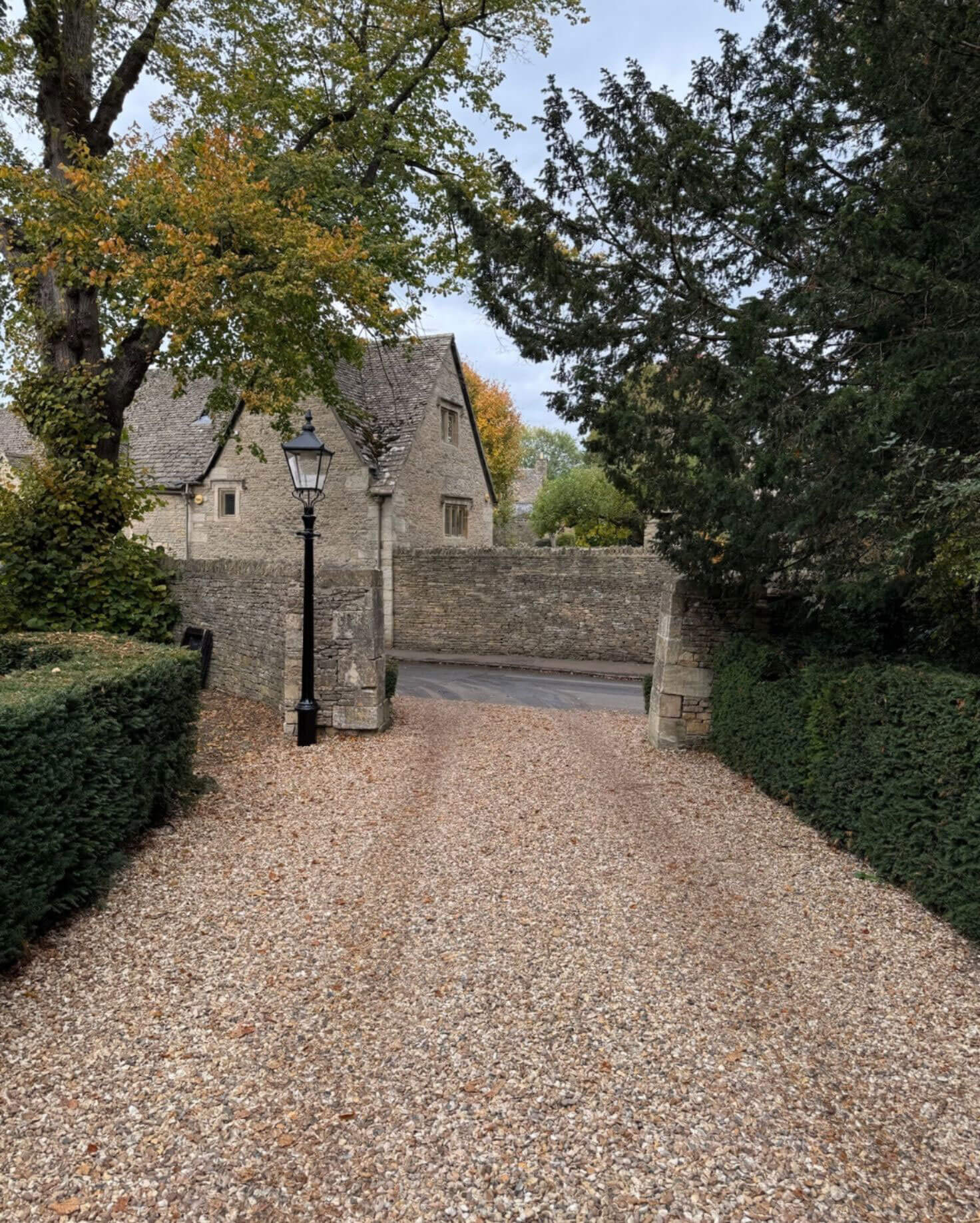 Leaf-covered driveway approaching a stone gatehouse