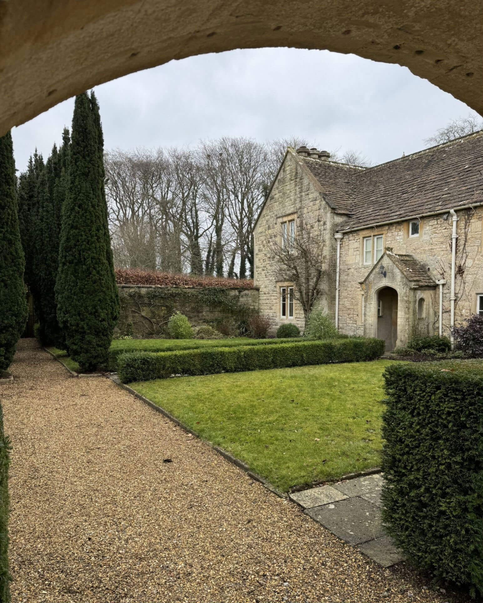 Manor courtyard and lawn viewed through a stone arch