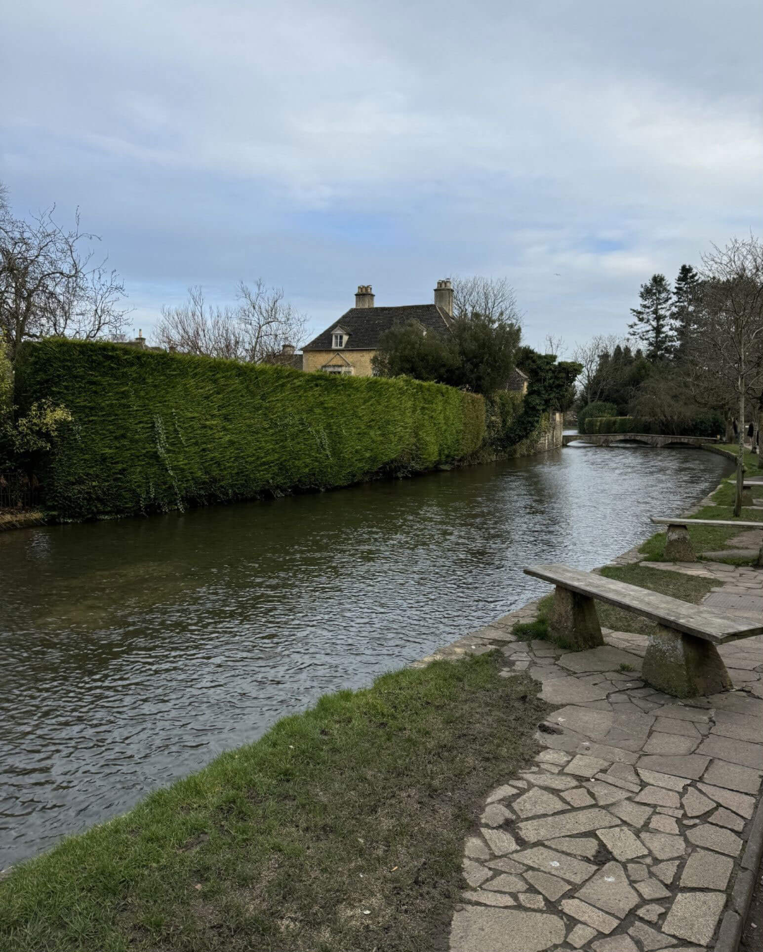 Quiet river bordered by a clipped hedge and stone path