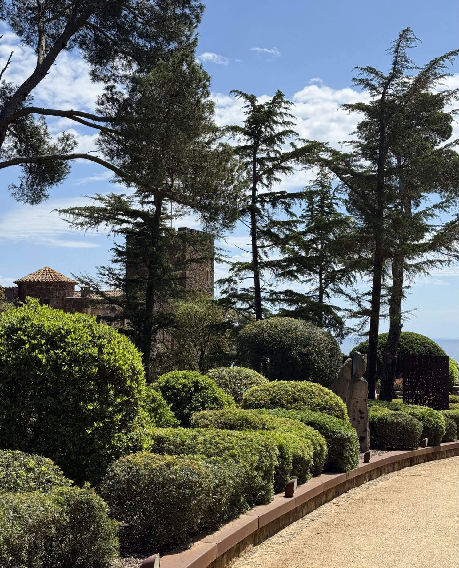 Clipped shrubs and mature trees beside a garden walk