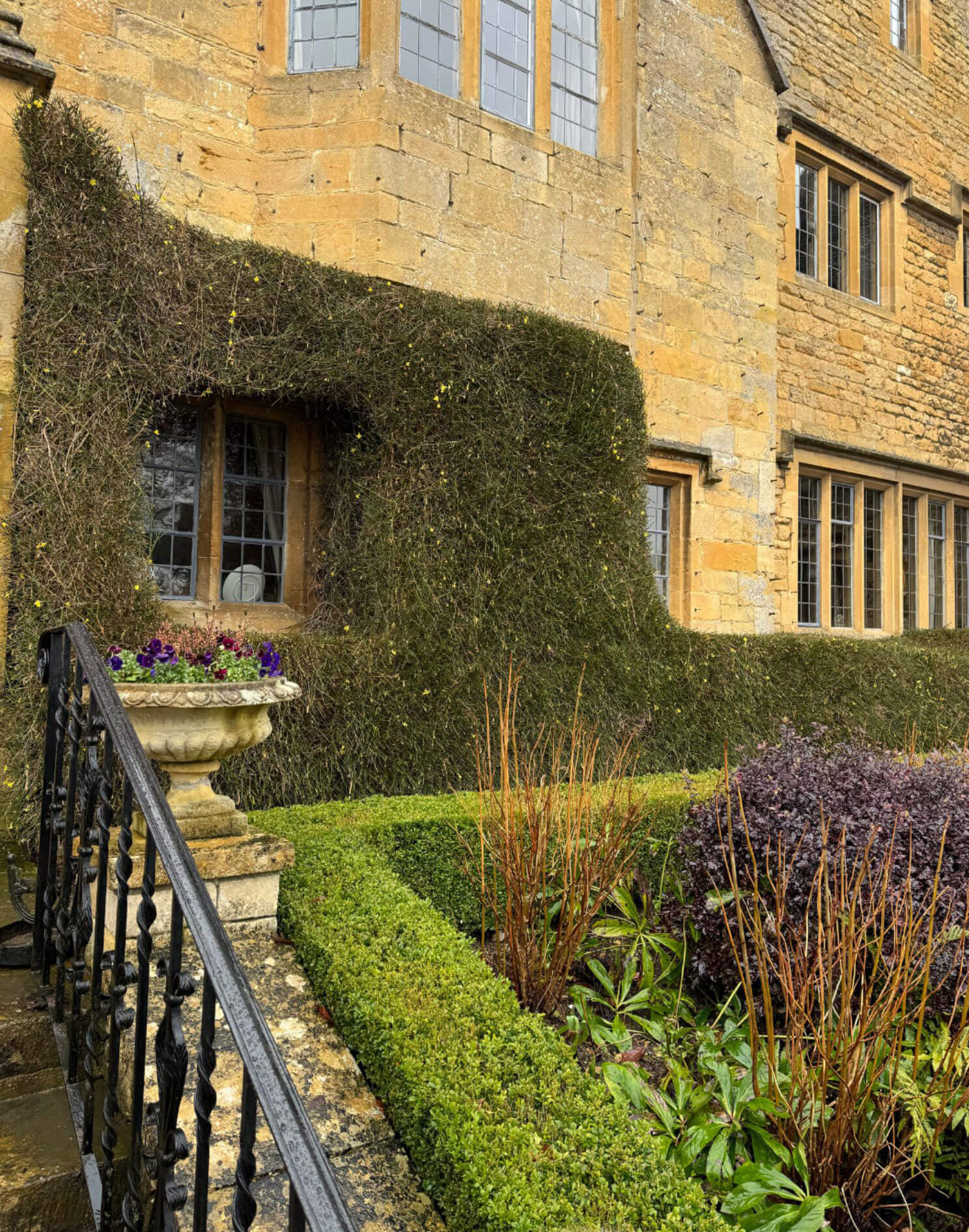 Clipped garden beds beside a stone bay window