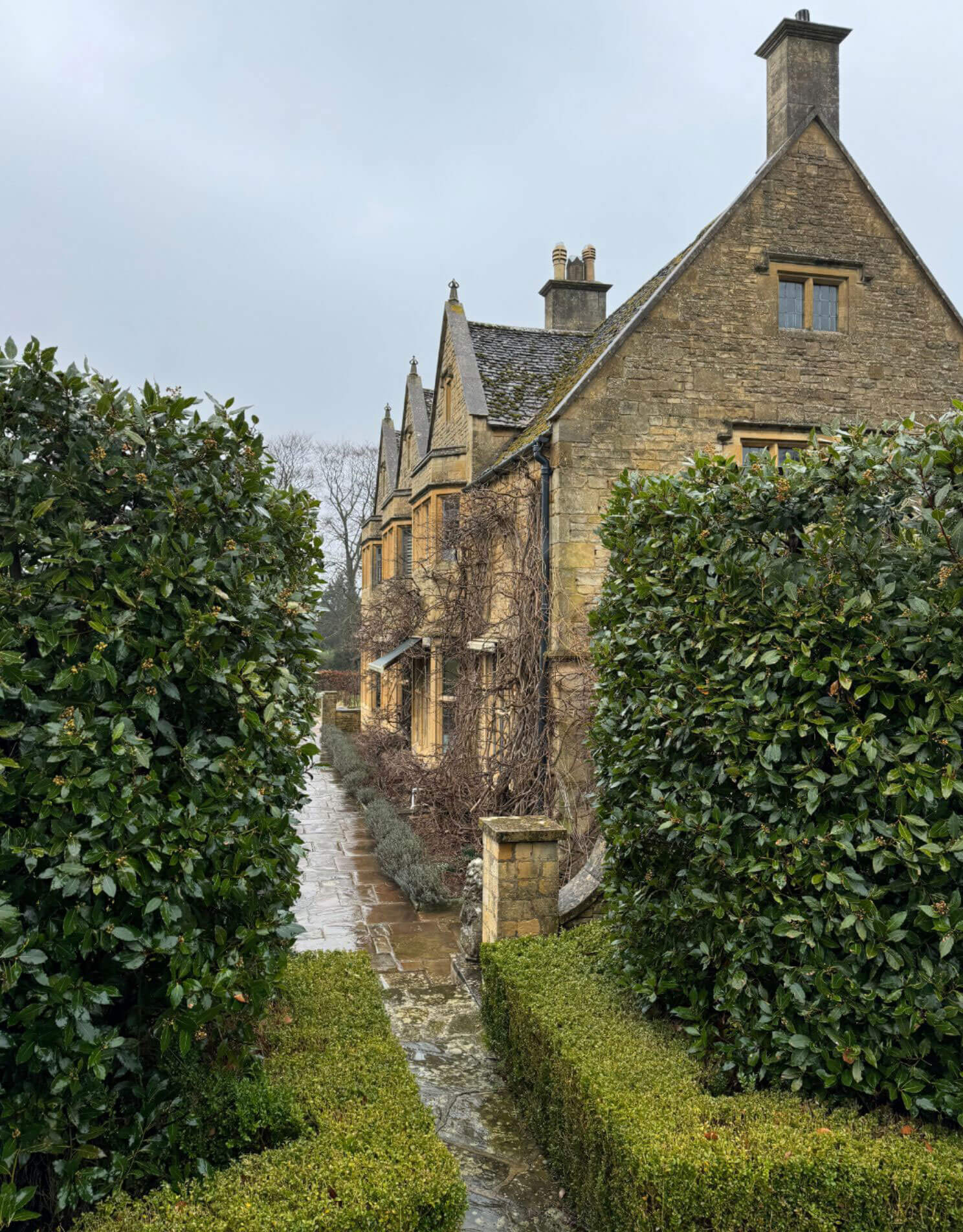 Stone manor wing beyond a clipped garden hedge