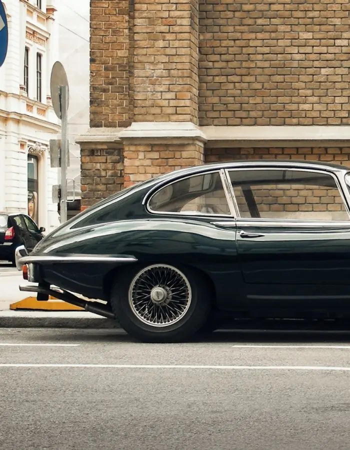 Classic green Jaguar E-type parked beside a brick building