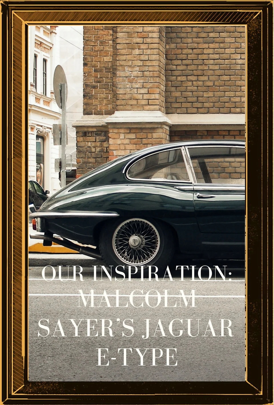 Side view of a dark Jaguar E-type parked outside a stone building, framed in gold