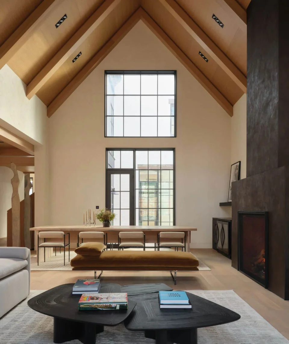 Sofas and sculptural coffee tables in a living room with exposed timber beams and tall windows