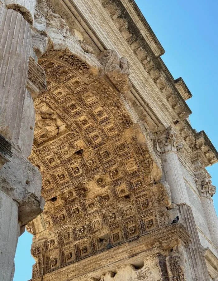 Looking up at an ornate stone arch with carved columns and a coffered ceiling