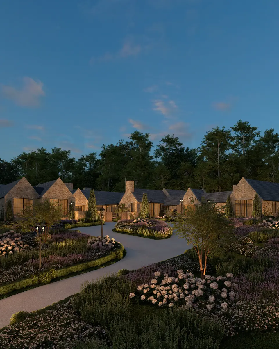 Stone country home with illuminated windows overlooking landscaped gardens at dusk